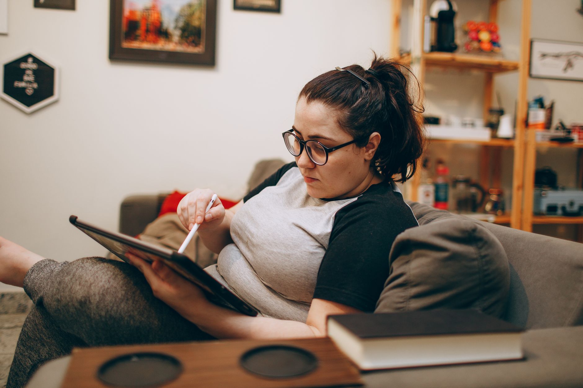 Woman relaxing on a couch while working from a tablet, the kind of flexible remote setup this admin side-income work allows.
