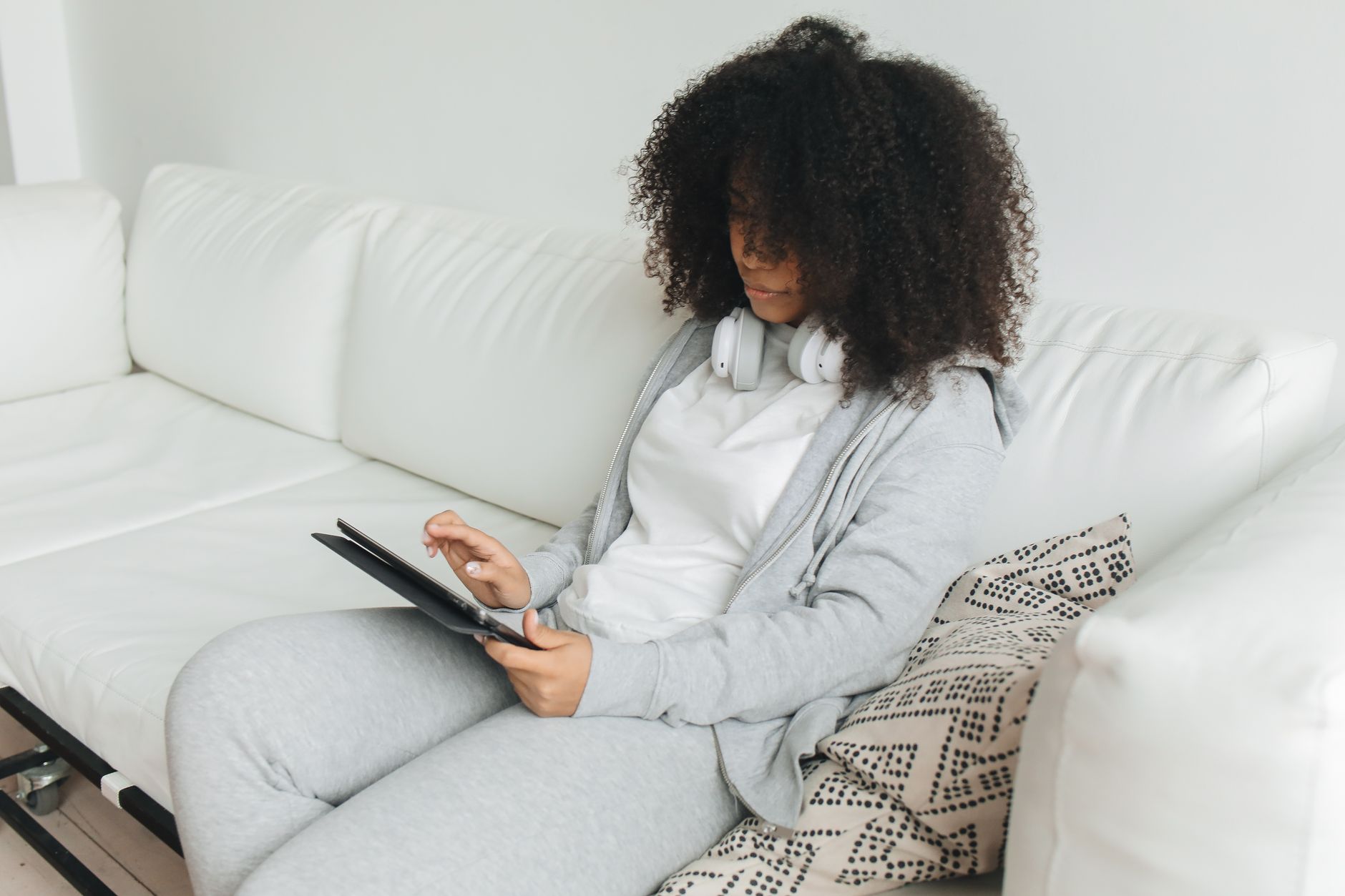 Woman with headphones using a tablet on a white sofa, working through a checklist-style routine.